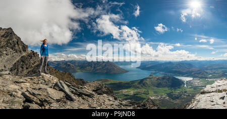 Weibliche Wanderer stehen auf Steine auf die Bergkette The Remarkables, mit Blick auf den Lake Wakatipu, Berge und Queenstown. Stockfoto