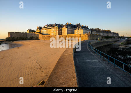 Die ummauerte Stadt Saint-Malo bei Sonnenuntergang mit Gebäuden in warmes Licht über der Mauer und der Mole Strand am Fuß der Stadtmauer hervorstehende gebadet. Stockfoto