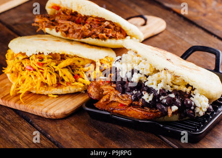 Venezolanische traditionelle Arepas frisch gemacht, mit 3 verschiedenen Füllungen Huhn Geschmack, gebratenes Fleisch und pabellon auf einer hölzernen Hintergrund Stockfoto