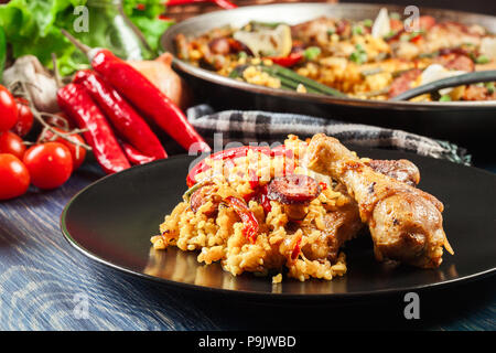 Traditionelle Paella mit Huhn Beine, Chorizo Wurst und Gemüse auf schwarzem Teller serviert. Spanische Küche Stockfoto