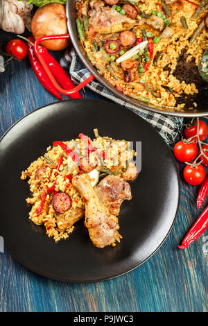 Traditionelle Paella mit Huhn Beine, Chorizo Wurst und Gemüse auf schwarzem Teller serviert. Spanische Küche. Ansicht von oben Stockfoto