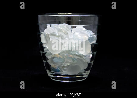 Ein kleiner tumbler Glas voll mit weissem und satiniert Marmor auf schwarzem Hintergrund. Stockfoto