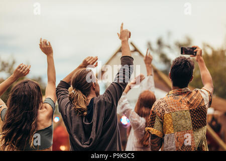 Rückansicht der Jugendlichen am Konzert. Gruppe der Männer und die Frau die Hände, und die Bilder an Music Festival. Stockfoto