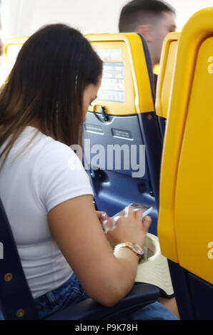 Eine Frau nimmt ihren Sitz und sendet eine SMS, während Sie in der Ebene, die Kabine auf einem Ryanair Flug sitzt Stockfoto