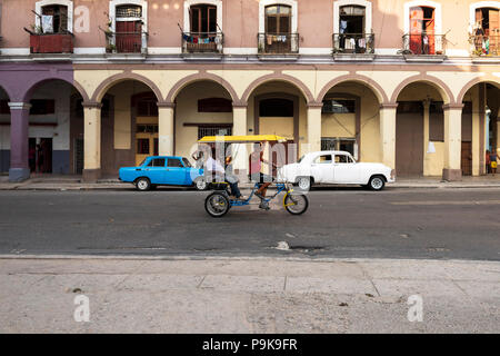 Mann, der fahrradrikscha mit Passagier im Vordergrund; Blau Lada und Wolga alte Autos auf der Straße in Havanna, Kuba geparkt. Stockfoto