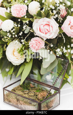 Zwei goldene Hochzeit Ringe auf moss Textur in vintage Glas, mit weißen Rosen dekoriert Stockfoto