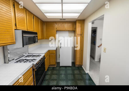 Alte 80er Jahre Wohnung Küche mit Eiche Schränke, Arbeitsplatten Fliesen, Gasherd und grünen Böden. Stockfoto
