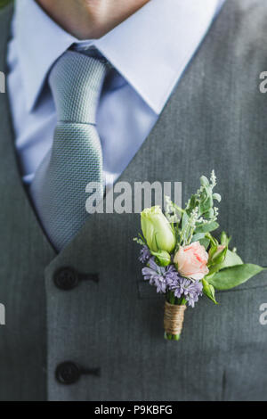 Bräutigam Anstecker mit kleinen Rosen und grünen Blättern auf grauen Anzug Stockfoto