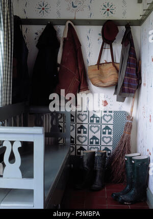 Kleidung und Taschen hängen an Peg-Schiene oben Gummistiefel in kleinen Häuschen Halle mit hellblauen Holzmöbeln vereinbaren Stockfoto