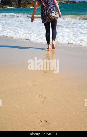 Frau geht barfuß am Strand, zum Meer in der Ferne verlassen Fußabdrücke auf dem nassen Sand, St Ives, Großbritannien Stockfoto