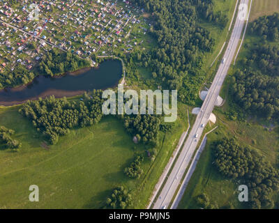 Blick von oben auf ein großes Dorf mit kleinen Häusern,, einen grünen Wald und ein großes Feld an einem warmen Sommertag. Hubschrauber Drohne erschossen. Stockfoto