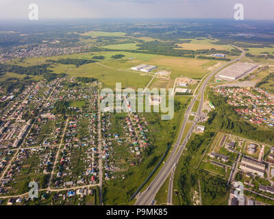 Hubschrauber Drohne erschossen. Blick von oben auf ein kleines Dorf, Motor Road, grünen Wald und einem großen Feld an einem warmen, sonnigen Sommertag Stockfoto