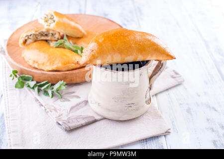 Frische hausgemachte Kuchen mit Käse und Grünen zum Frühstück. Teil Torten. Auf einer hölzernen Platte und auf einem weißen Hintergrund. Eine Tasse Tee. Freier Platz für Text oder Werbung Stockfoto