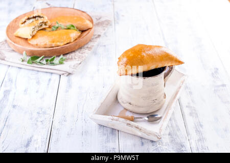 Frische hausgemachte Kuchen mit Käse und Grünen zum Frühstück. Teil Torten. Auf einer hölzernen Platte und auf einem weißen Hintergrund. Eine Tasse Tee. Freier Platz für Text oder Werbung Stockfoto