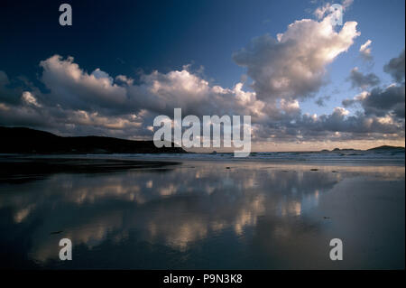 Sonnenlicht piercing Gewitterwolken leuchtet eine Leere und abgelegenen Strand. Stockfoto