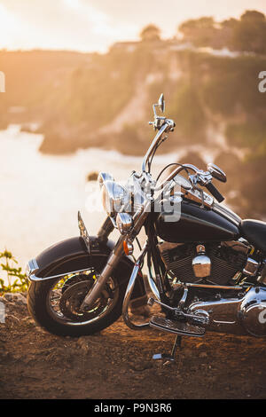 Alte Oldtimer Motorrad stehen am Rand der Klippe in warmes Sonnenlicht bei Sonnenaufgang, glänzend Details zu Fahrrad close-up Stockfoto