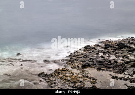 Eine lange Belichtung Foto einer felsigen Küste mit Strand, Steine und Pools treffen geisterhafte Wellen des Ozeans. Konzept Frieden Gelassenheit. Kopieren Sie Platz. Stockfoto