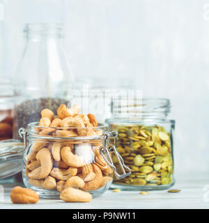 Verschiedene Nüsse und Samen, die in Gläsern über weiße Holztisch vor weißem Hintergrund. Das Konzept der vegetarischen und Bio-Lebensmittel. Stockfoto