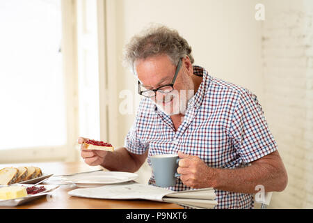 Portrait von Happy senior alter Mann mit grauen Haaren lesen die Zeitung beim Frühstück und trinken einen Kaffee in glückliches Alter Ruhestand Konzept Stockfoto