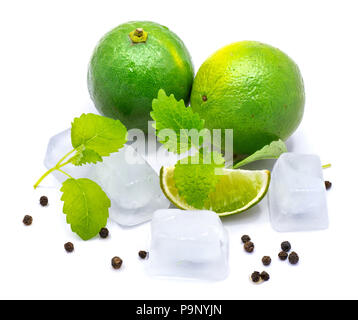 Zwei ganze Limes, eine Scheibe, Zitronenmelisse Blätter, klare Eiswürfel und Pfeffer auf weißem Hintergrund Stockfoto