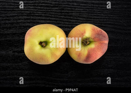 Zwei frische reife Saturn Pfirsiche flatlay auf schwarz Holz Hintergrund Stockfoto