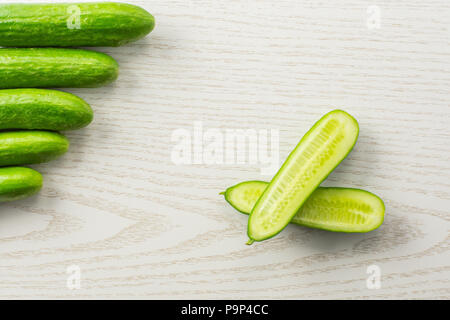 Fünf frische Mini Gurken und einem Schnitt in zwei Hälften flatlay auf grau Holz Hintergrund Stockfoto