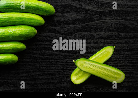 Fünf frische Mini Gurken und einem Schnitt in zwei Hälften flatlay auf schwarz Holz Hintergrund Stockfoto