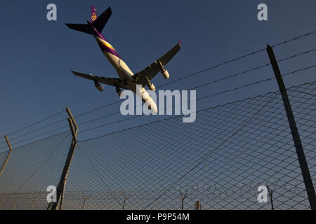 Der Airbus A 340 zivilen jet Flugzeug von Thai Airways fliegt über sicherheitszaun als es landet am Internationalen Flughafen Malpensa, Mailand, Italien Stockfoto