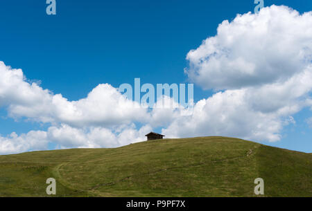 Kleines Holzhaus auf einem grasbewachsenen Hügel und alpine Ridge unter einem blauen Himmel mit weißen Wolken in den Schweizer Alpen Stockfoto