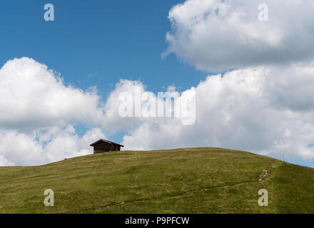 Kleines Holzhaus auf einem grasbewachsenen Hügel und alpine Ridge unter einem blauen Himmel mit weißen Wolken in den Schweizer Alpen Stockfoto