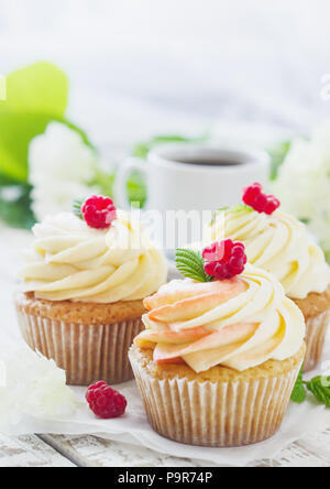 Zarte Vanille Cupcakes mit Sahne und Himbeeren auf einem weißen Holz- Hintergrund Stockfoto