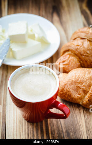 Tasse duftenden Kaffee und Croissants mit Butter auf einem Holztisch. Ansicht von oben Stockfoto