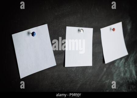 Drei weiße Aufkleber auf Schwarzes Brett mit farbigen Noppen verstiftet Stockfoto