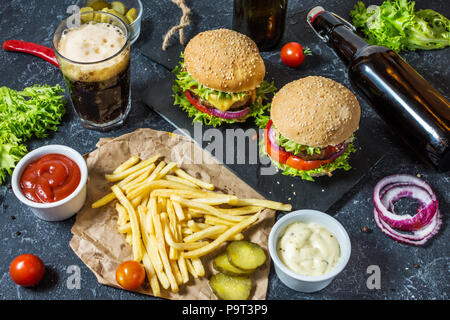 Hausgemachte Burger mit Rindfleisch und mit Bratkartoffeln und Glas kalten dunklen Bier auf Tisch aus Stein. Stockfoto