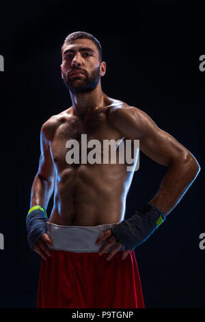 Stattliche athletischer Kerl in einem rote Shorts auf schwarzem Hintergrund. Der Boxer ist das Abrufen von seinem Atem nach dem Üben Haken und bläst. Professionelle Kämpfer. Stockfoto