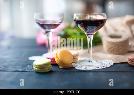 Zwei Gläser Rotwein. Ein Blumenstrauß aus Rosen in braunem Papier. Farbe Gebäck Makkaroni. In der Nähe der Fenster. Freier Platz für Text oder Postkarten Stockfoto