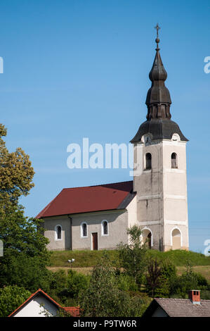 Slowenien: Eine der typischen slowenischen Dörfer mit einer Kirche auf einem Hügel, grüne Wiesen, Bäumen und kultivierten Flächen in der Landschaft Stockfoto