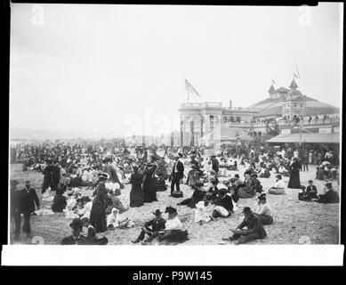 . Englisch: Massen von Menschen auf dem Strand in der Nähe der Badewanne Haus in Long Beach, CA.1906 Foto: viele Leute (die meist nicht in Badekleidung, sondern voll bekleidet) Sonnenbaden am Strand vor dem 2-stöckiges Haus mit großen Portico in Long Beach, CA. 1906. Eine amerikanische Flagge auf dem Dach. Der Ozean ist nicht sichtbar. Teil der Stadt ist im Hintergrund sichtbar. Lesbare Zeichen gehören: ice cream's "erriam Salon', 'wissenschaftliche Erfrischungen', 'SHandleser', 'Pop Corn', 'Tin.... Rufnummer: CHS--1991 Dateiname: CHS--1991 Abdeckung Datum: ca. 1906 Teil der Sammlung: Kalifornien Historische Stockfoto