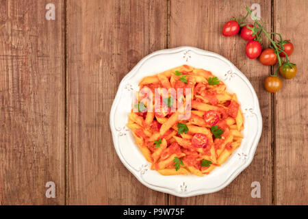 Ein Foto von einem Teller Pasta mit Tomatensauce. Penne Rigate mit Cherry Tomaten und frische Petersilie, auf einem dunklen rustikalen Textur mit Cop Stockfoto