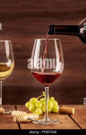 Rotwein wird in ein Glas von einer Flasche gegossen, auf einem dunklen Hintergrund, mit einem Platz für Text und Trauben im verschwommenen Hintergrund. Design Template fo Stockfoto