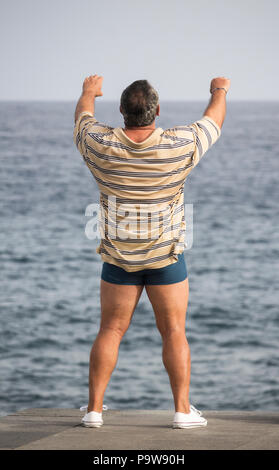Ansicht der Rückseite des reifer Mann Durchführen von Tai Chi mit Blick auf das Meer Stockfoto