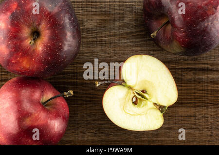 Red Delicious drei Äpfel und eine Hälfte flatlay auf braunem Holz Hintergrund Stockfoto