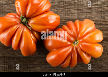 Zwei Rindfleisch Tomaten (Schmetterling und Blume Formen) Ansicht von oben isoliert auf braunem Holz Hintergrund eine große reife rote Bündchen flatlay Stockfoto