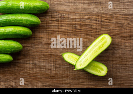 Fünf frische Mini Gurken und einem Schnitt in zwei Hälften flatlay auf braunem Holz Hintergrund Stockfoto