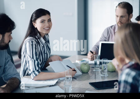 Diskussion in der Gruppe. Fröhliche schöne Frau mit Ihrem Notebook und am Tisch sitzen, bei einem Treffen mit ihren Kollegen Stockfoto