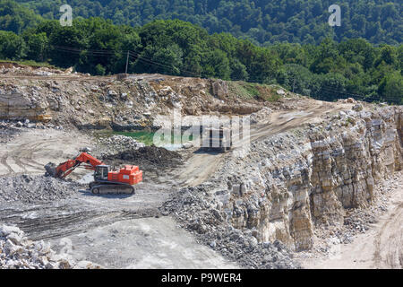 Der Tieflöffel und großen Lkw-Arbeit in der Gips Steinbruch im Sommer. Industrielle Landschaft Stockfoto