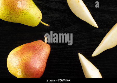 Gruppe von zwei ganze drei Scheiben frische rote Birne forelle Vielfalt flatlay auf schwarzem Holz Stockfoto