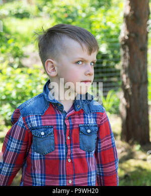 6-jähriger Junge schaut schief die Linse im Frühling Garten Stockfoto