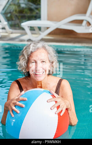 Vitale ältere Frau mit einem bunten Ball in den Pool im Urlaub Stockfoto