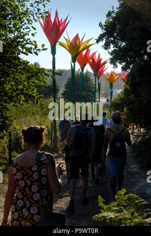 Eine Reihe von riesigen, bunten Blumen Lampen ist mit einer Hintergrundbeleuchtung ausgestattet, die von der späten Nachmittagssonne als Menschen zurück entlang der Pfad vom Sonnenaufgang Arena entfernt. Stockfoto